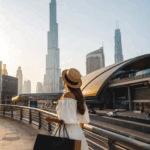 Traveler with shopping bags exploring Dubai near a metro station with Burj Khalifa skyline during golden hour.